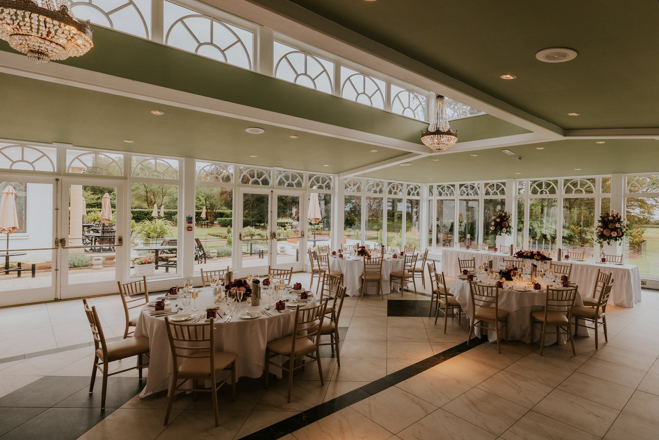 Wedding reception tables with white linen, flowers and candles beneath chandeliers at Lochgreen House Hotel.