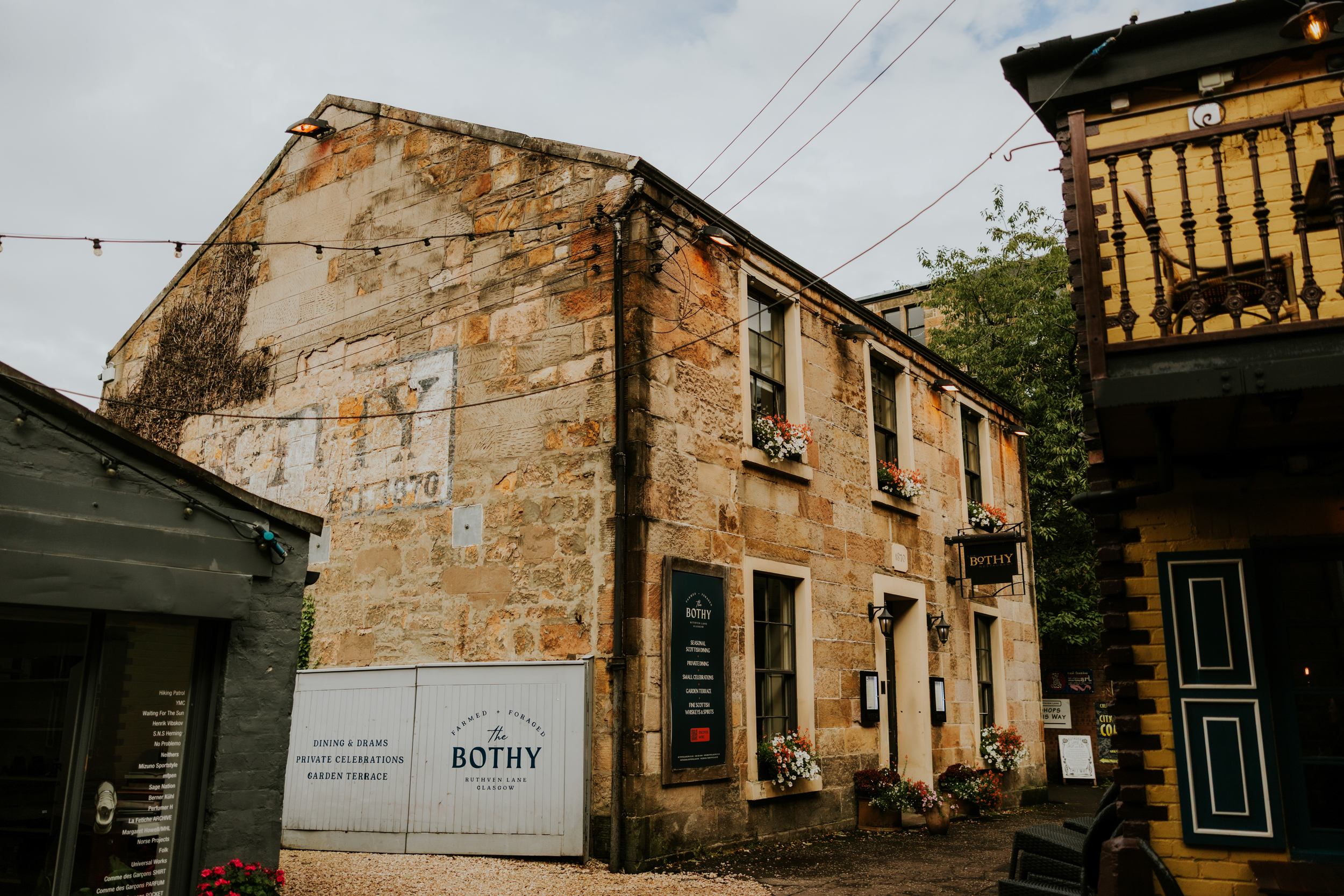 Stone exterior of The Bothy in Glasgow with windows, flower boxes, hanging lights and entrance sign.