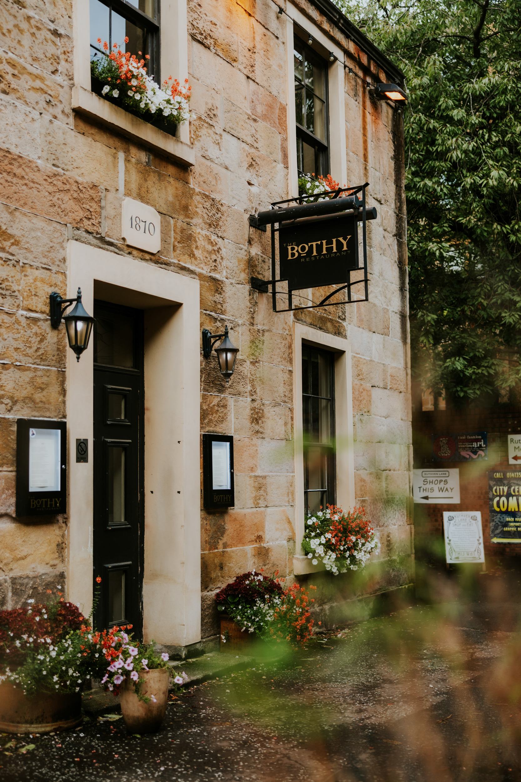 Stone-front entrance with a hanging 'Bothy' sign and window flower boxes outside the restaurant.